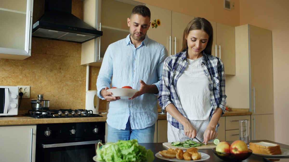 Happy young couple embracing and talking in the kitchen while cooking breakfast at home in the morning
